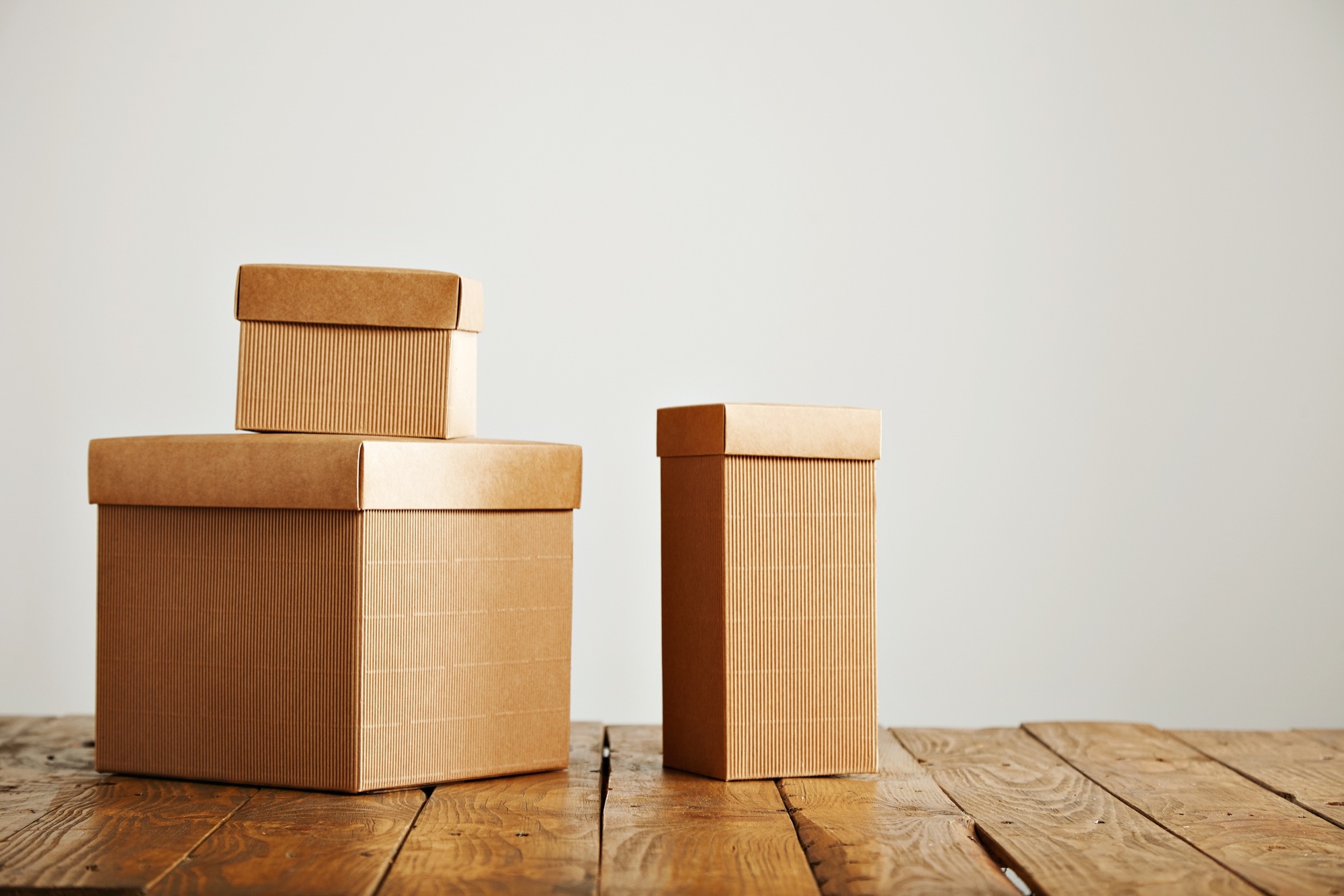 three-different-sized-beige-cardboard-boxes-arranged-on-top-of-a-brown-rustic-table-in-a-studio-with-white-walls